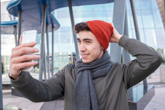 Young man wearing knit hat taking selfie through mobile phone in city