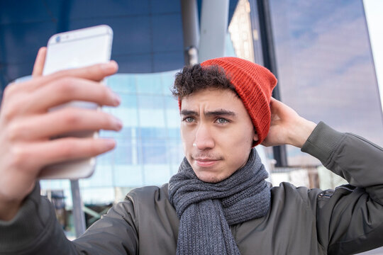 Young man adjusting knit while taking selfie through smart phone in city