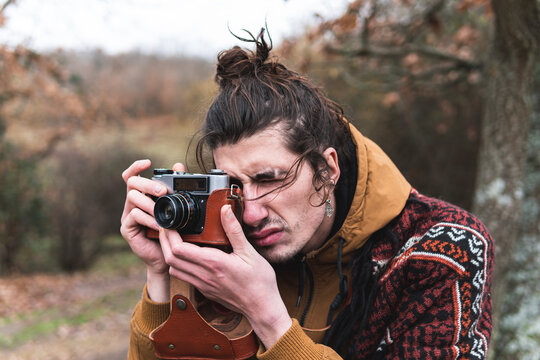 Young man photographing Autumn landscape with vintage camera