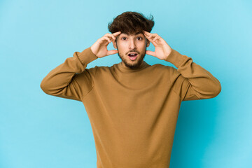 Naklejka premium Young arab man on blue background receiving a pleasant surprise, excited and raising hands.