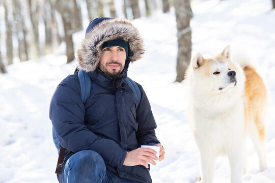 Mid adult man and akita dog looking away while holding coffee cup in snow