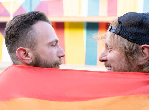 Close-up of romantic gay men with rainbow flag looking at each other