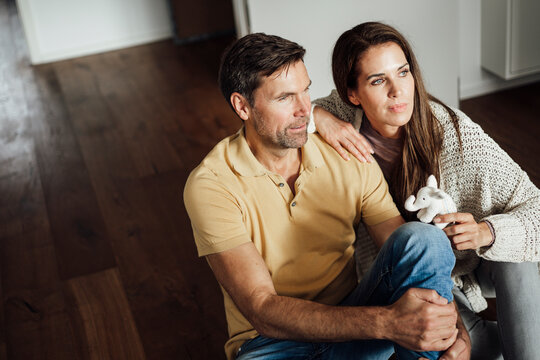 Mature woman holding elephant stuffed toy while day dreaming with man in apartment