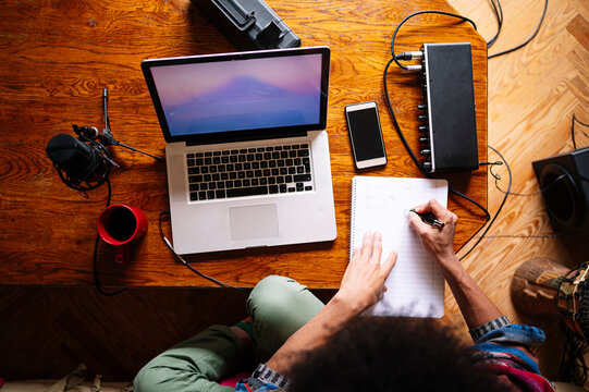 Male Afro musician writing notes by laptop on table at home