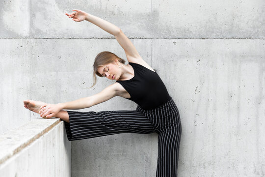 Dancer in black striped pants stretching in front of concrete wall