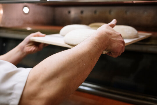 Male baker keeping bread dough in oven at bakery