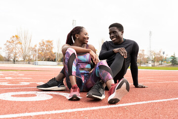 Happy male and female athlete sitting on running track against clear sky