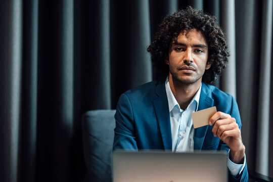Confident young male professional holding credit card while sitting with laptop at office