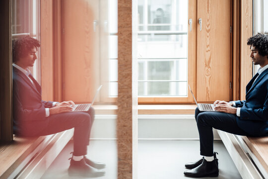 Businessman using laptop with reflection of himself on glass at workplace