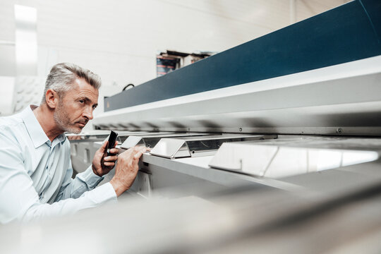 Mature Inspector Examining Machine While Standing At Industry