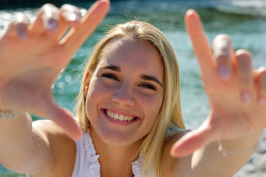 Cheerful young woman showing finger frame while standing against lakeshore on sunny day