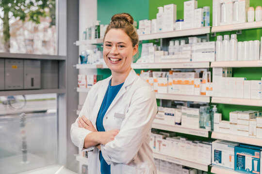 Happy pharmacist with arms crossed standing in chemist shop