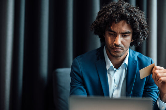 Confident young businessman using laptop while holding credit card at office