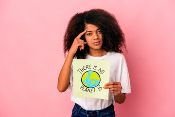 Young african american curly woman holding a planet message on a placard pointing temple with finger, thinking, focused on a task.