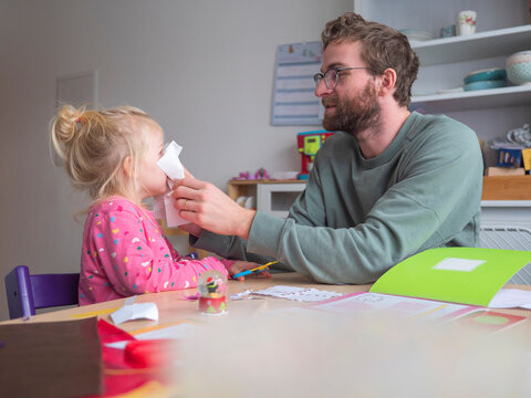 Playful father holding paper on daughter's while sitting at table