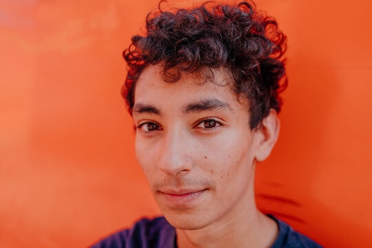 Close-up portrait of handsome man with curly hair against orange wall