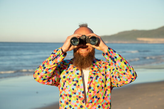 Smiling man looking through binocular while standing against sea