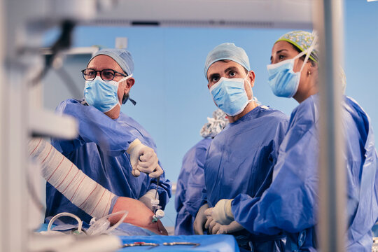 Surgeon team wearing protective face mask operating shoulder arthroscopic surgery while standing in operation room