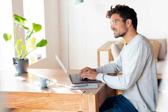 Man wearing eyeglasses looking away while sitting with laptop at home office