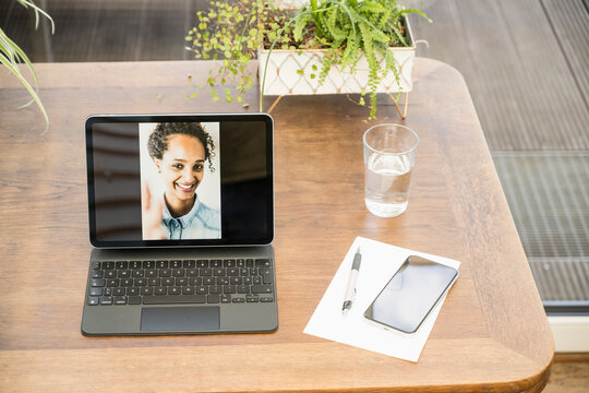Photograph of young woman on digital tablet screen by glass on table at home