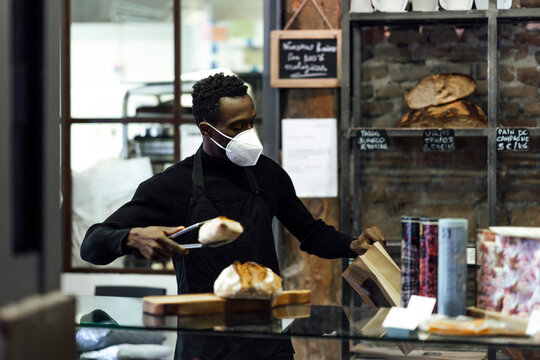 Salesman wearing face mask packing bread while standing at bakery