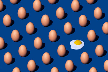 Pattern made with whole eggs and one poached egg on dark blue background. Minimal flat lay composition. Food wallpaper.