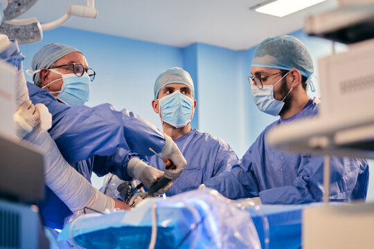 Male doctors operating surgery with surgical equipment while standing in operating room during COVID-19