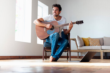 Smiling man playing guitar while sitting on chair at home