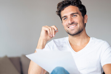 Mid adult man with paper smiling while looking away sitting at home