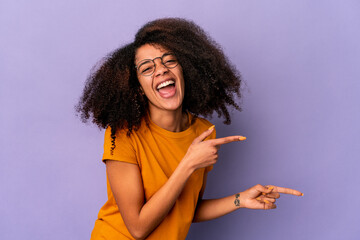 Young african american curly woman isolated on purple background pointing with forefingers to a copy space, expressing excitement and desire.