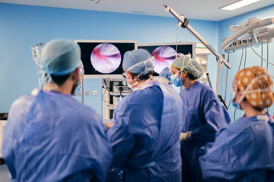 Doctors operating surgery through computer screen while standing at operation room during COVID-19
