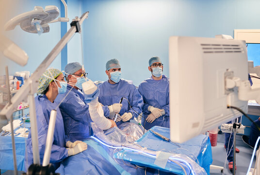 Surgeons in face mask and medical scrubs operating arthroscopic surgery while standing at operation room during COVID-19