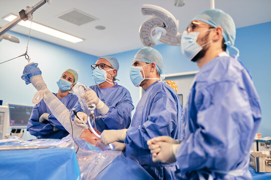 Surgeon with endoscope equipment operating shoulder arthroscopy while standing with colleague in operating room during COVID-19