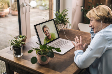 Happy senior woman on video call with grandson while sitting at table in home