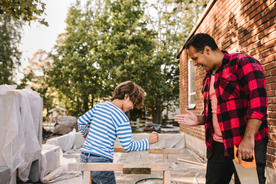 Son breaking wooden plank with hand while smiling father gesturing outside house