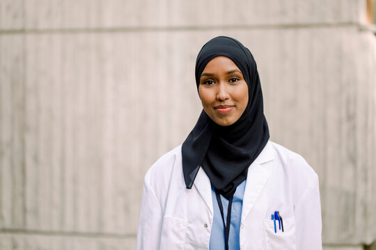 Portrait Of Smiling Nurse Wearing Hijab While Standing Against Wall In Hospital