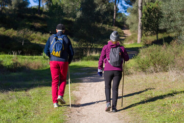 A mature couple walking along a country path. General shot. Two people hiking in the mountain with sportswear, backpack, and hiking tracking sticks. Healthy sports lifestyle concept.