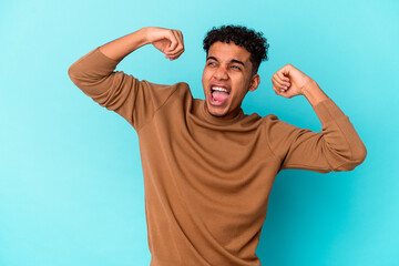 Naklejka premium Young african american curly man isolated on blue celebrating a special day, jumps and raise arms with energy.