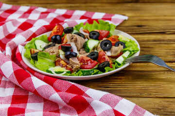 Tasty tuna salad with lettuce, black olives and fresh vegetables on wooden table