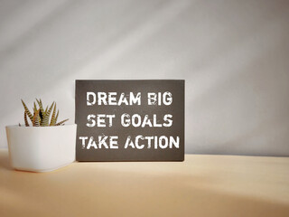 Motivational and inspirational text - DREAM BIG SET GOALS TAKE ACTION on black paper background. Stock photo.