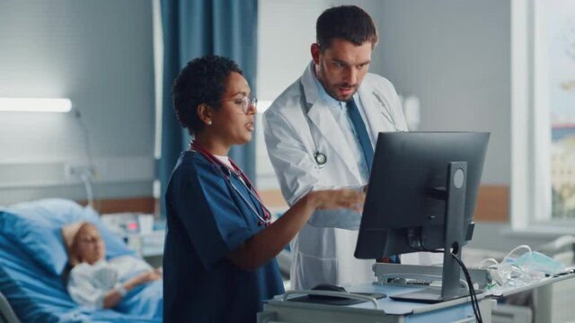 Hospital Ward: Caucasian Doctor Talks With Professional Black Head Nurse, They Use High-Tech Computer. In Background Patient in Bed Recovering after Successful Surgery. Health Care Specialists