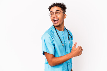 Young african american curly nurse man isolated points with thumb finger away, laughing and carefree.