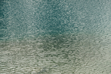 Texture of green blue calm water of lake. Meditative ripples on water surface. Nature minimal background of green blue lake with golden shine. Natural backdrop of lake fragment with clear azure water.