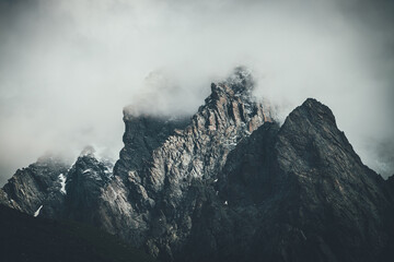 Dark atmospheric surreal landscape with dark rocky mountain top in low clouds in gray cloudy sky....
