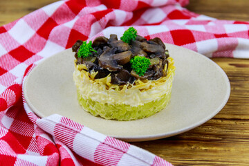 Tasty layered salad with roasted mushrooms, potato, eggs, cheese and mayonnaise on wooden table