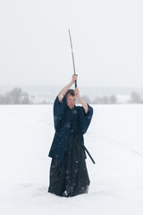 samurai warrior stands with sword and staff in the middle of an empty winter field