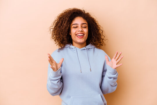 Young african american woman isolated on beige background laughs out loudly keeping hand on chest.