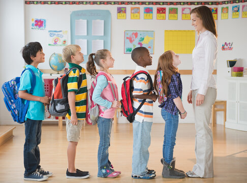 School children (8-9) with female teacher standing in row in classroom