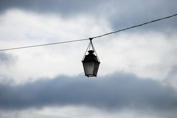 Obraz premium Closeup of vintage street light suspended on cable in the street on cloudy sky background