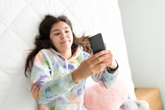 Pretty teen girl holding her phone and resting in bed
